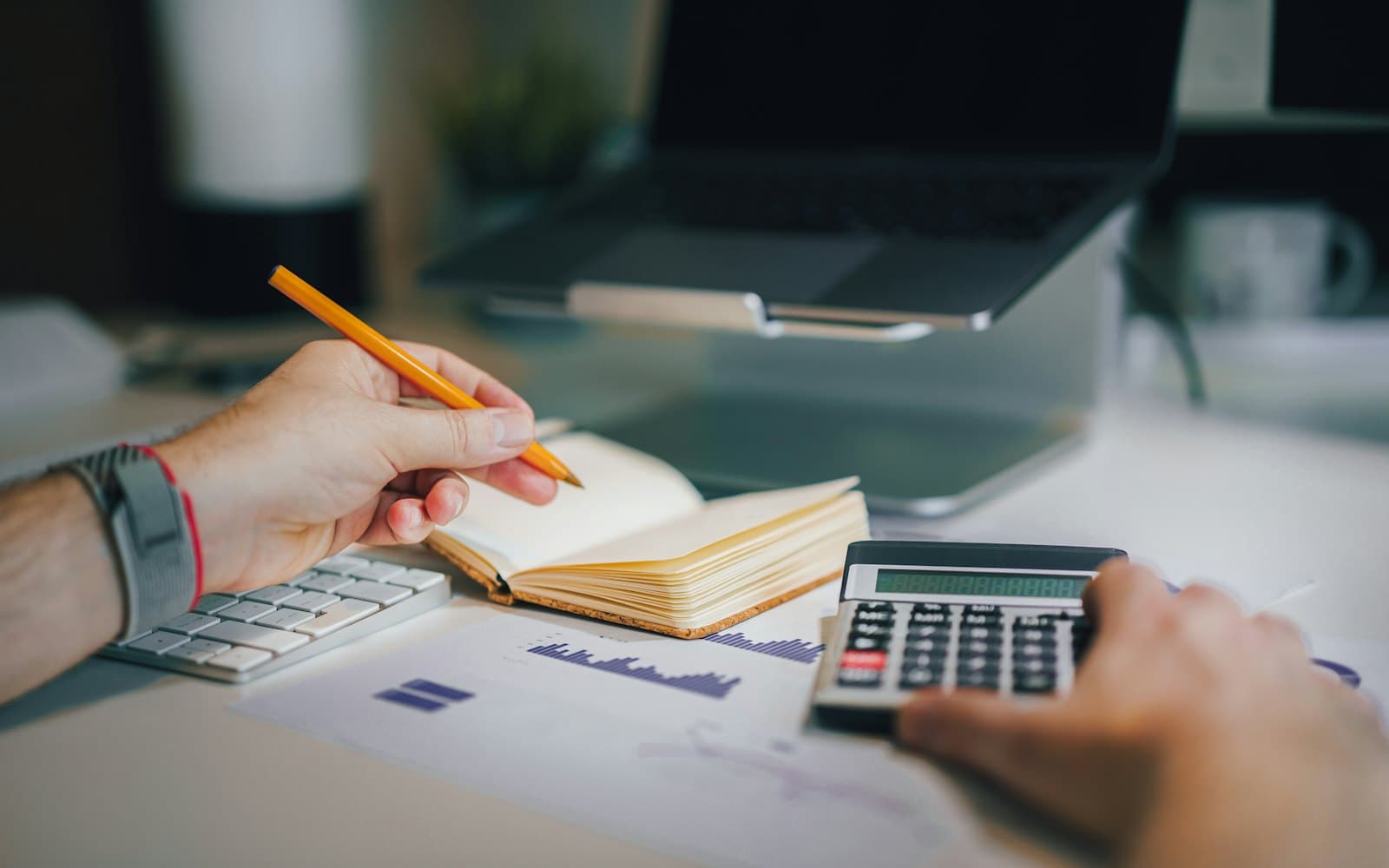 Mãos com lápis e calculadora sobre um caderno de anotações